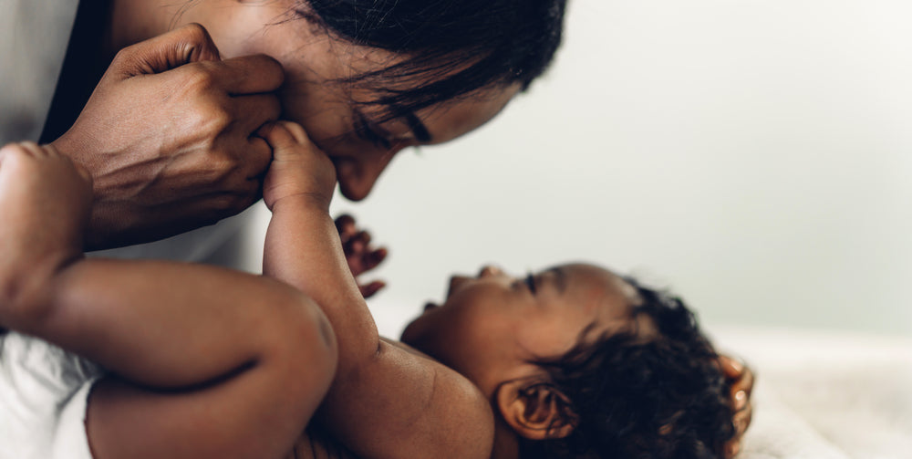 Mother playing with her baby on the bed. Both the mother and the baby are smiling.