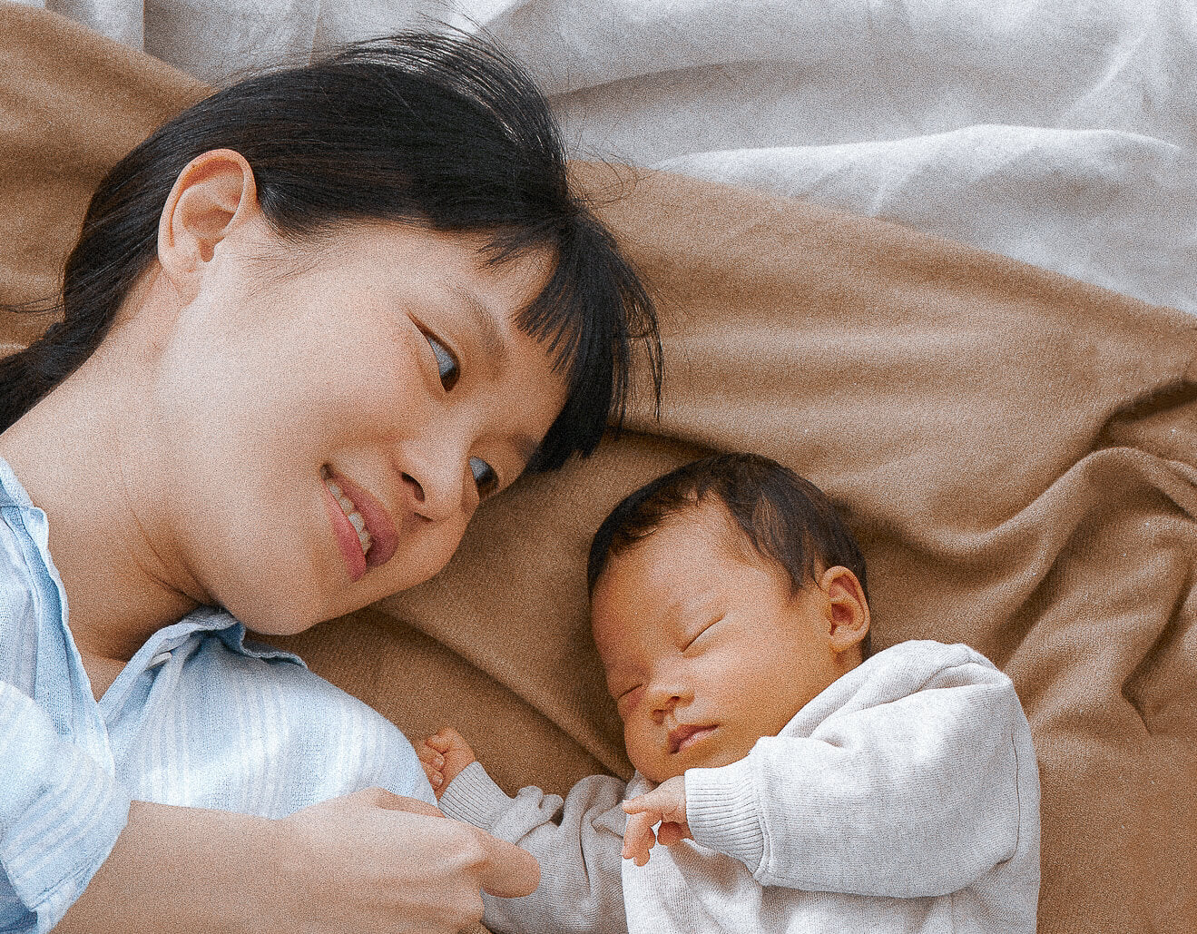 Asian women laying next to her baby on a bed